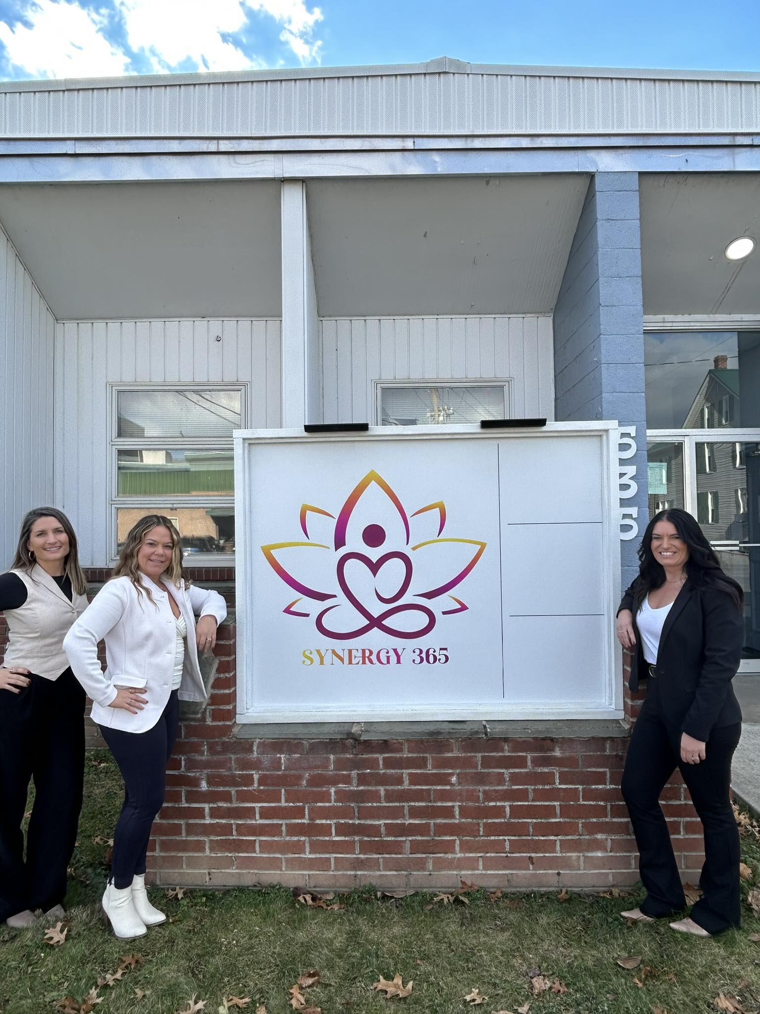 Three Synergy 365 wellness team members standing confidently beside the company sign